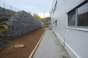 Obrzek 4: Pohled na oprnou gabionovou stnu, za zd vlevo frekventovan silnice, vpravo vrobn hala, ped zd zelen ps