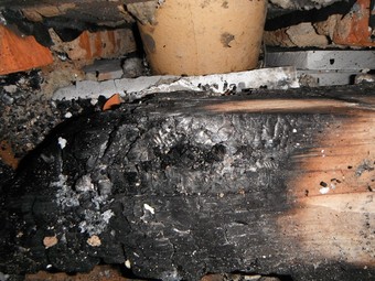 Obrázek 8 – Nad neizolovaným kouřovodem od krbu byla vedena pozednice dřevěného krovu (viz schéma). Odstínění bylo provedeno tenkou nehořlavou deskou, která se porušila. K požáru domu došlo po dvou letech používání krbu samovznícením pozednice.