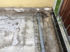 Detail podkladního betonu v místě okapu, beton se drolí, okapnice pod ním je v protispádu