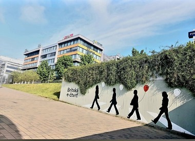 Foto&nbsp;5 Mural v&nbsp;pěší trase administrativního komplexu. Velkoformátový mural oživuje pěší trasu a&nbsp;posiluje vizuální orientaci v&nbsp;území. Jasné grafické prvky zvyšují čitelnost prostoru a&nbsp;podporují přirozený dohled v&nbsp;exponované části areálu.